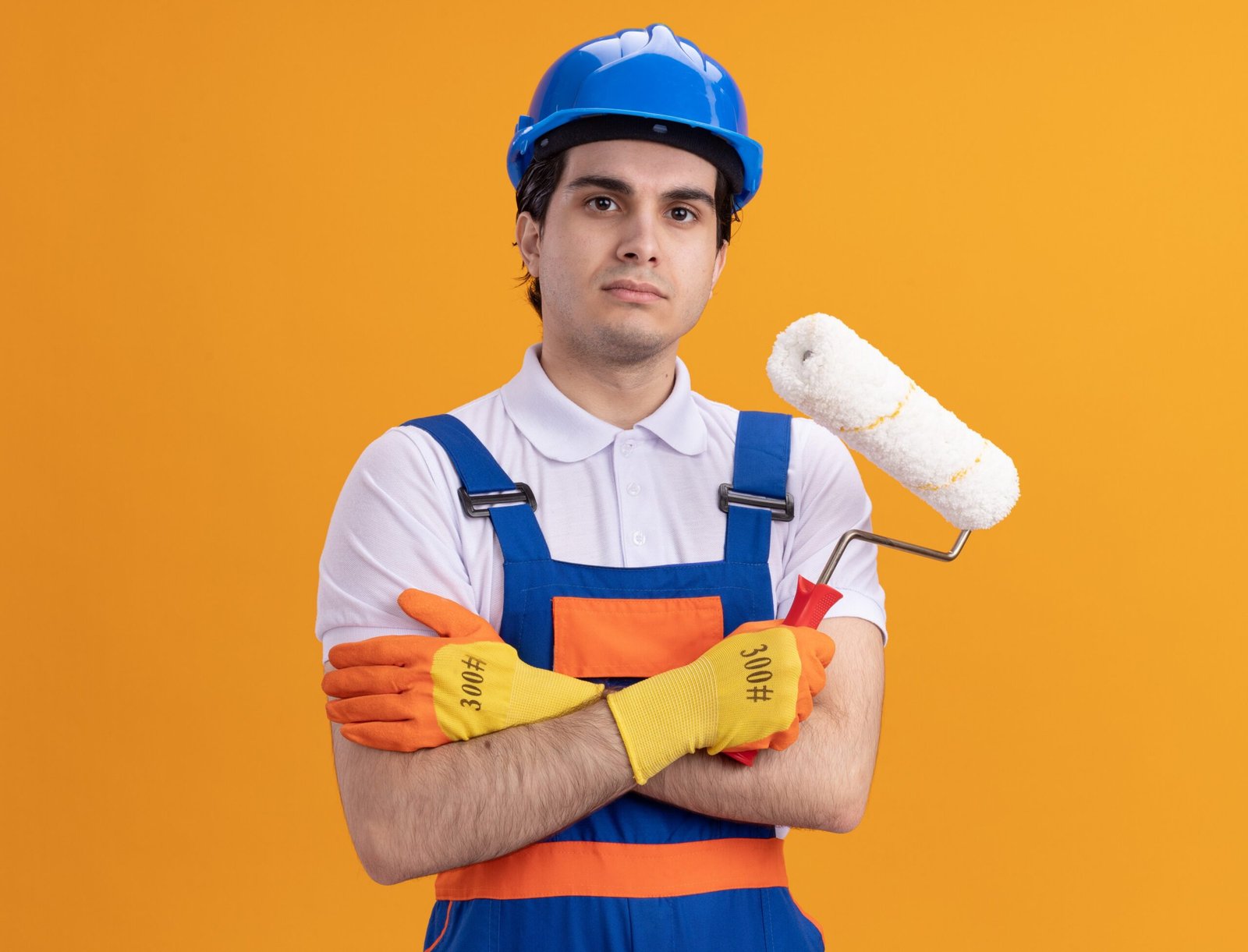 angry-young-builder-man-construction-uniform-safety-helmet-wearing-rubber-gloves-holding-paint-roller-looking-front-with-serious-confident-expression-standing-orange-wall (1)